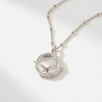 The Mermaid's Coin - a 2cm round gold disc pendant featuring a bold seashell motif and the Latin inscription 'Fluctuat nec mergitur', handcrafted by Dainty London.