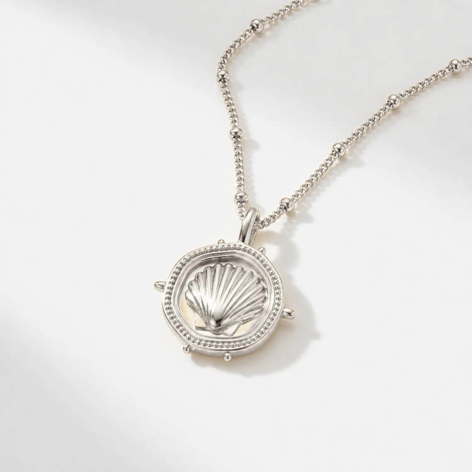 The Mermaid's Coin - a 2cm round gold disc pendant featuring a bold seashell motif and the Latin inscription 'Fluctuat nec mergitur', handcrafted by Dainty London.
