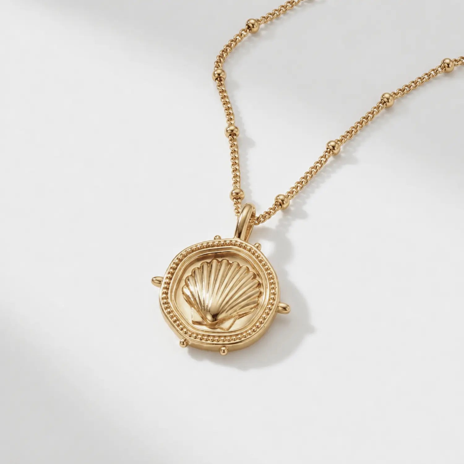 The Mermaid's Coin - a 2cm round gold disc pendant featuring a bold seashell motif and the Latin inscription 'Fluctuat nec mergitur', handcrafted by Dainty London.