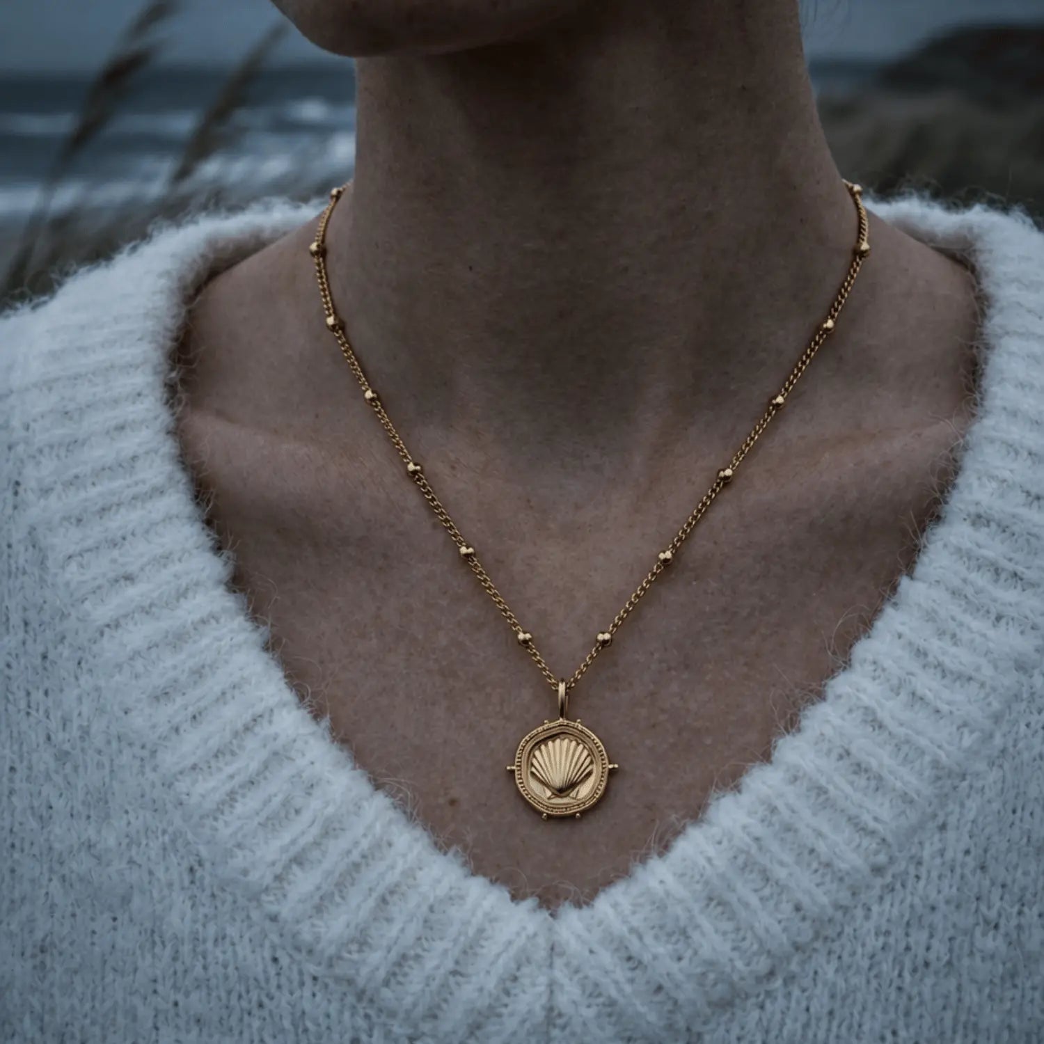 The Mermaid's Coin - a 2cm round gold disc pendant featuring a bold seashell motif and the Latin inscription 'Fluctuat nec mergitur', handcrafted by Dainty London.