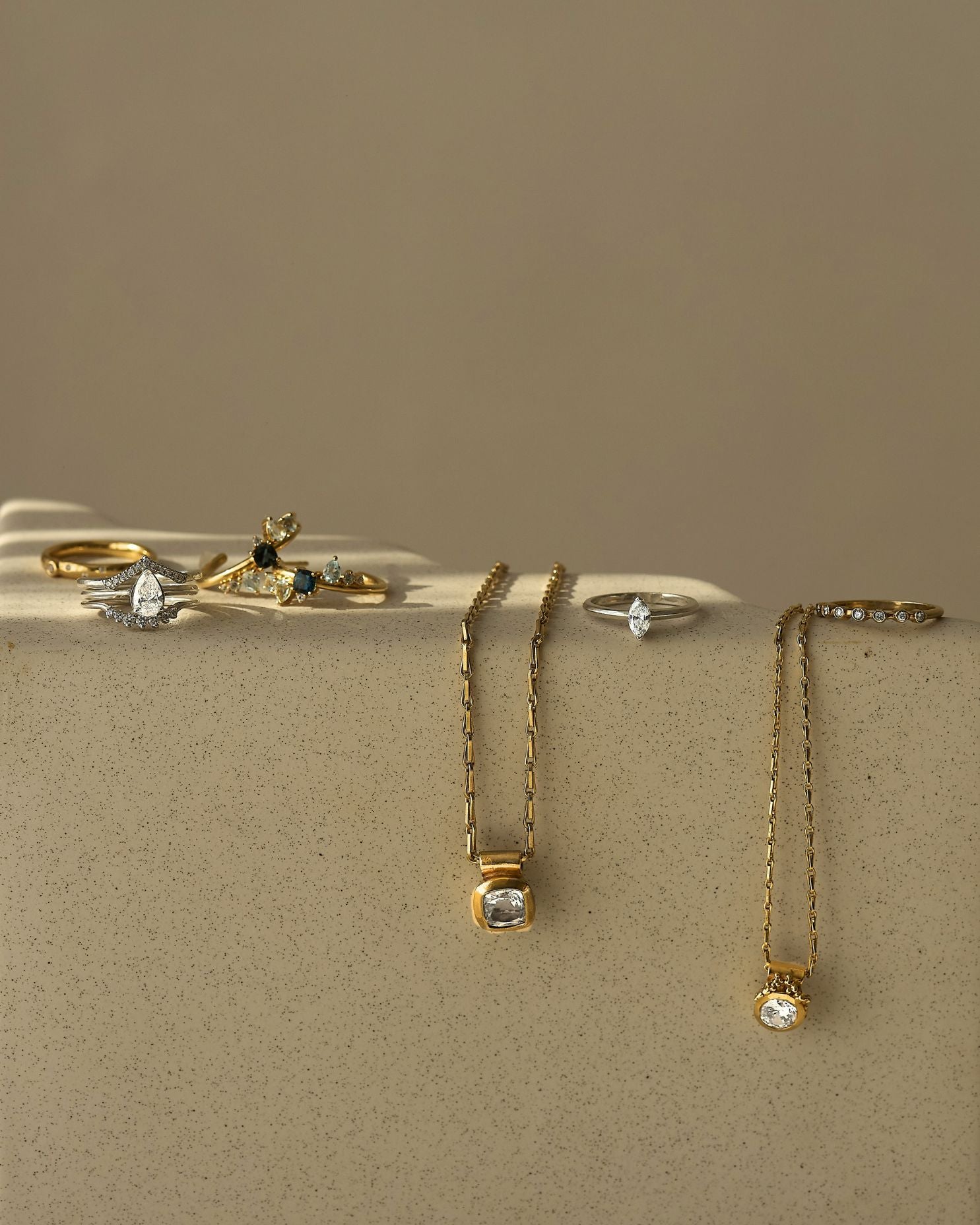 Gold jewelry including rings and necklaces on a beige surface with a neutral background