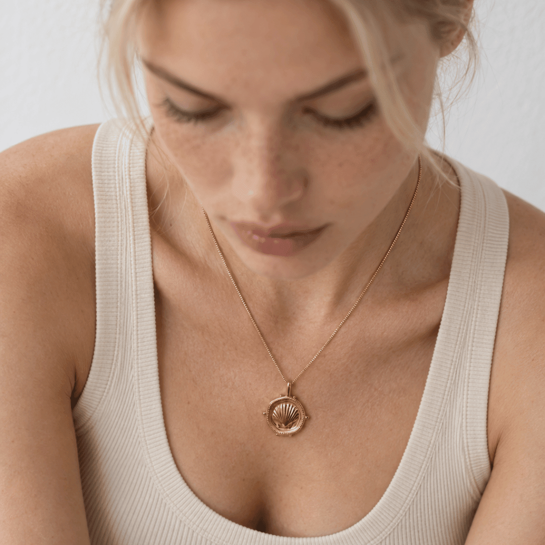 The Mermaid's Coin - a 2cm round gold disc pendant featuring a bold seashell motif and the Latin inscription 'Fluctuat nec mergitur', handcrafted by Dainty London.