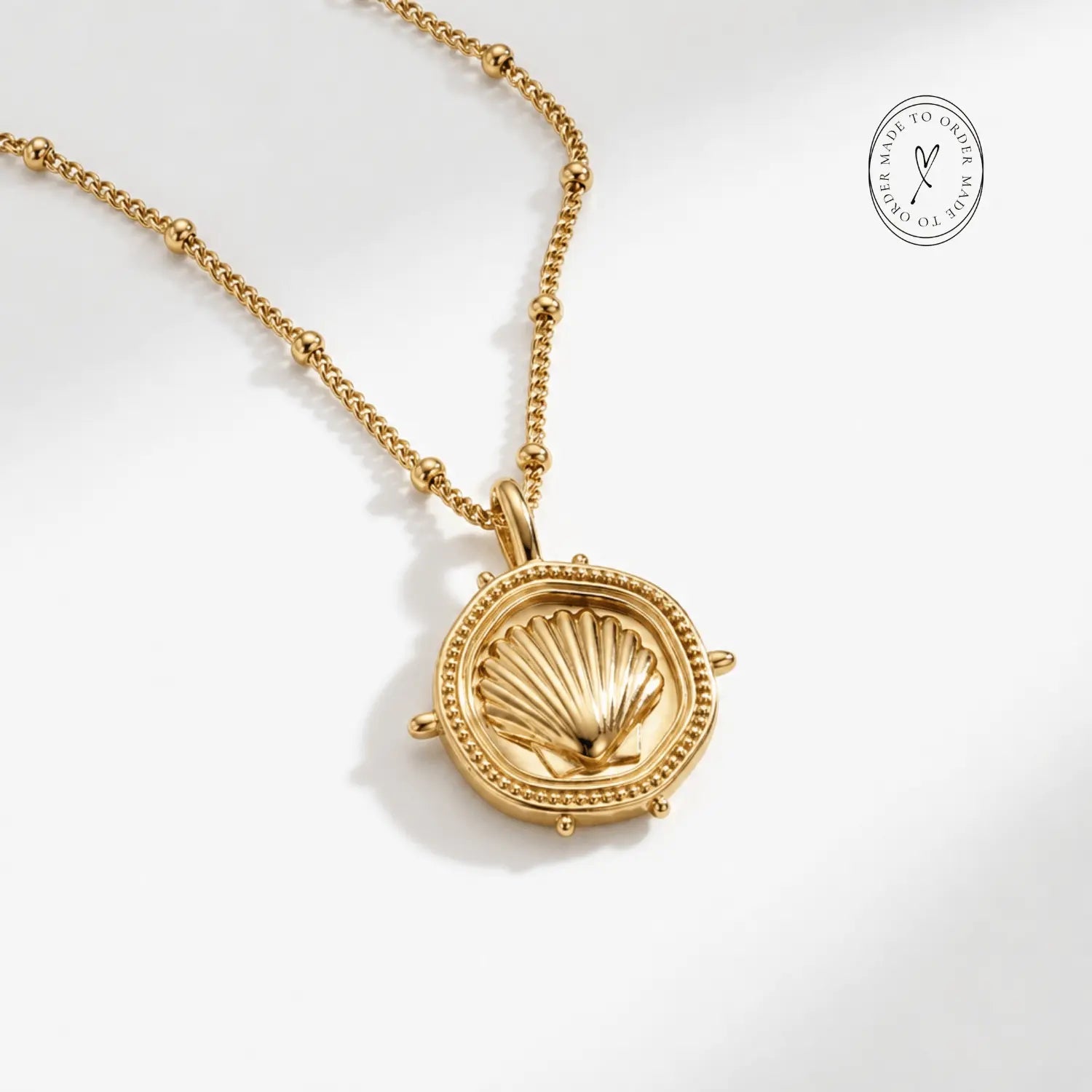 The Mermaid's Coin - a 2cm round gold disc pendant featuring a bold seashell motif and the Latin inscription 'Fluctuat nec mergitur', handcrafted by Dainty London.
