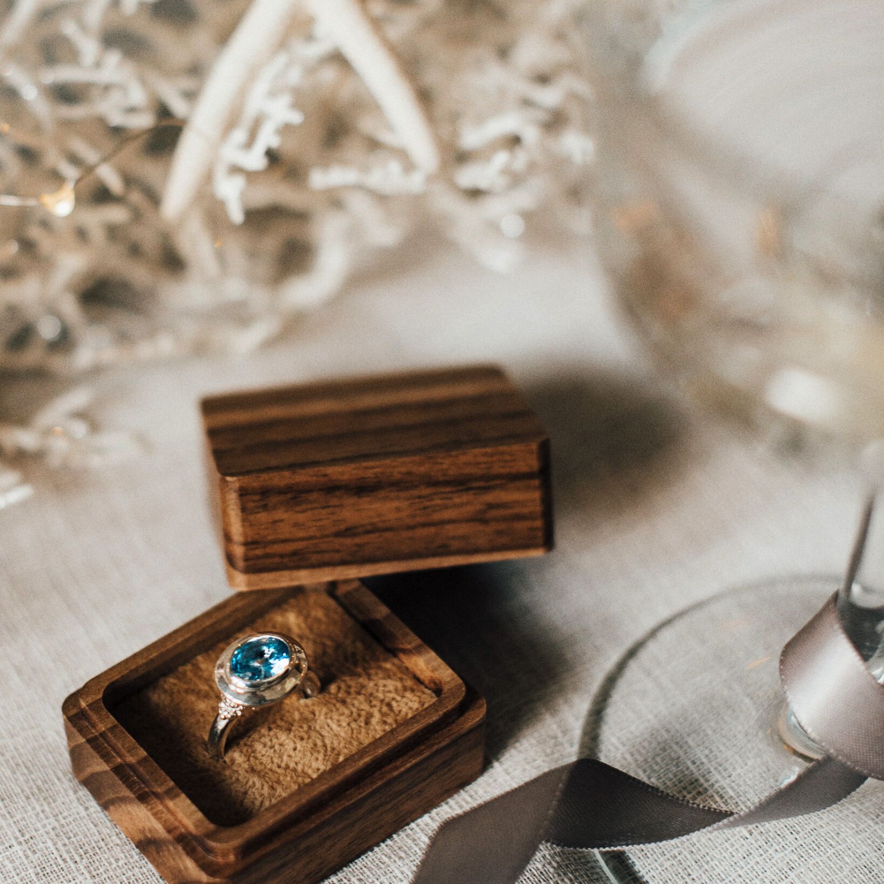 Wooden ring box with a ring featuring a blue gemstone on a textured surface.
